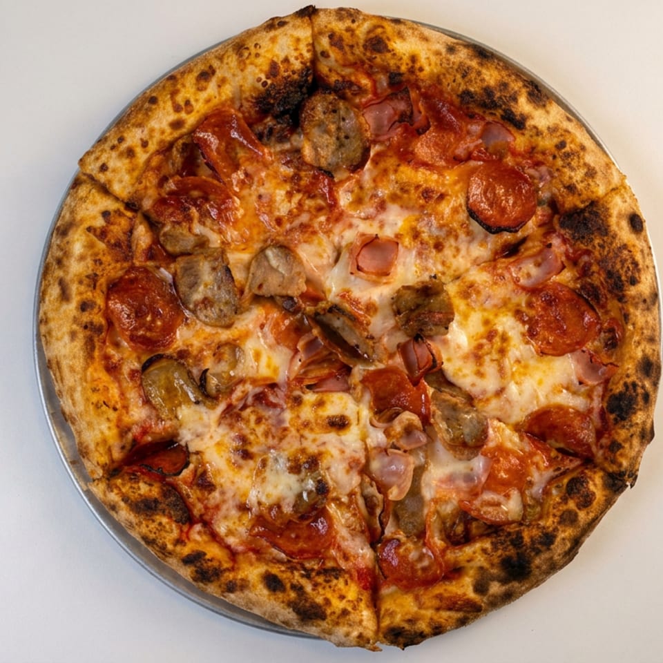 Overhead view of a charred-crust pizza topped with melted cheese, pepperoni, sausage, ham, and mushrooms.