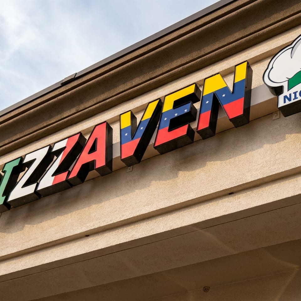 Exterior sign for Pizzavenue Night & Day restaurant mounted on a beige building under a partly cloudy sky.